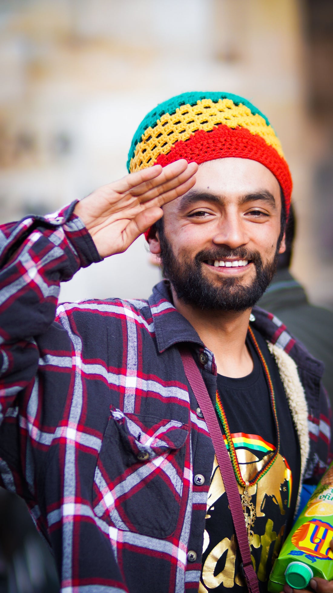 A Rastafarian man wearing a red, gold, and green knitted tam raises his hand in salute, symbolizing the enduring spirit, pride, and global legacy of Jamaican reggae culture.
