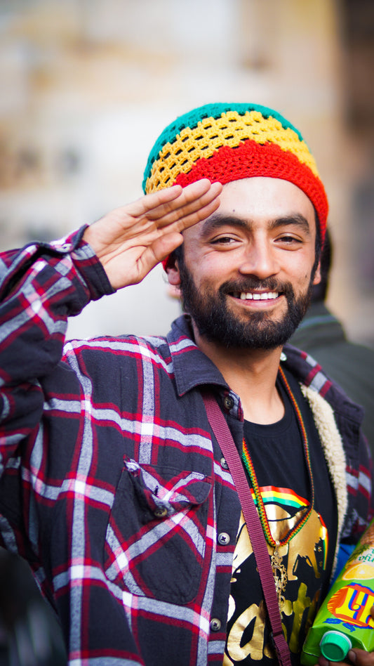A Rastafarian man wearing a red, gold, and green knitted tam raises his hand in salute, symbolizing the enduring spirit, pride, and global legacy of Jamaican reggae culture.